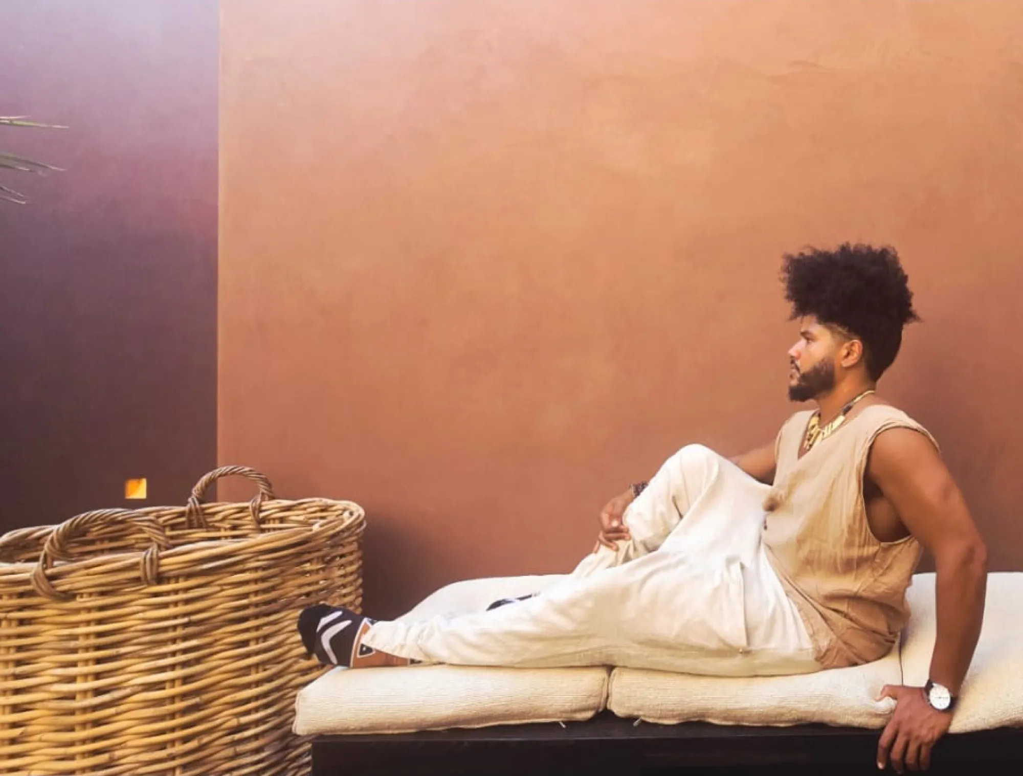Benjamin Urbaez relaxing in earth-toned linen outfit against terracotta wall, Dominican-American global touring musician portrait