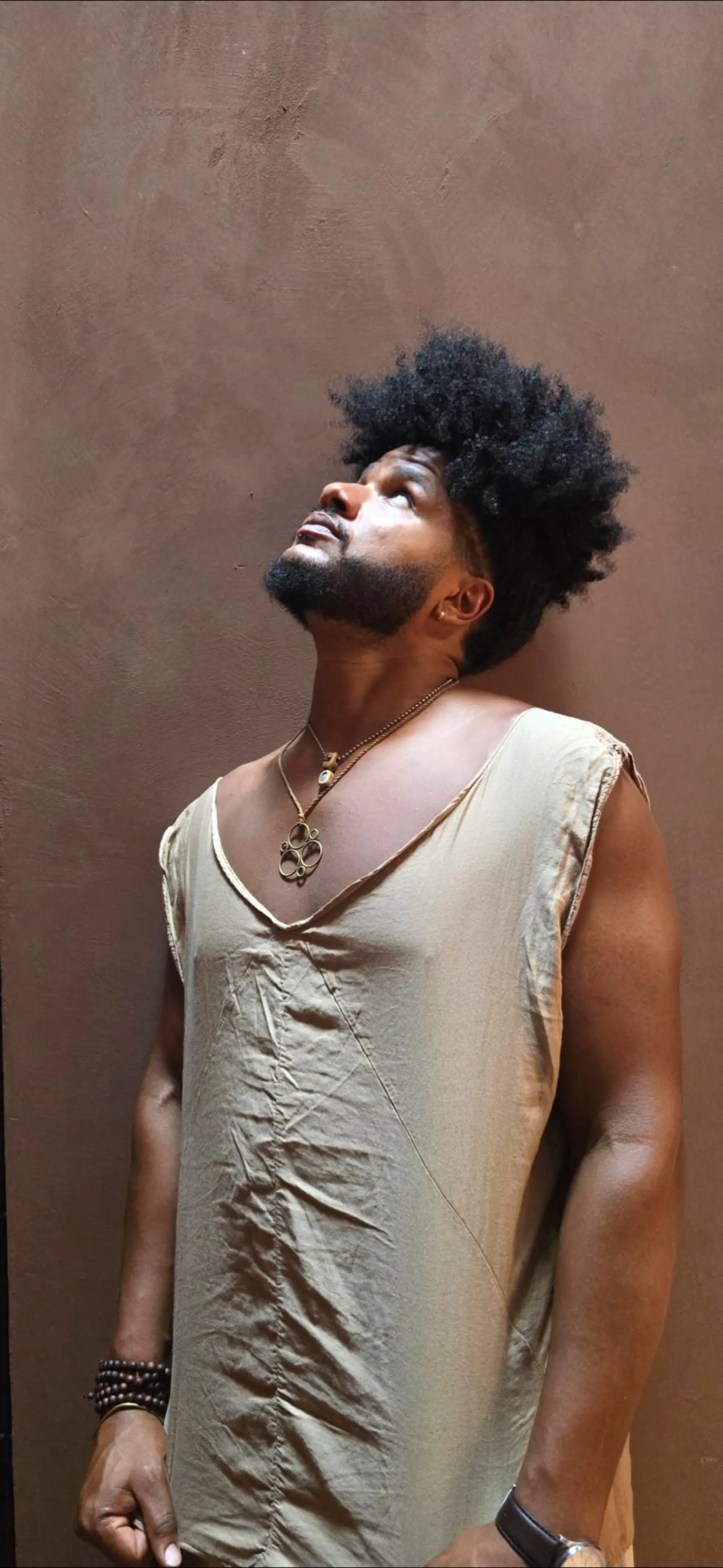 Benjamin Urbaez looking upward in earth-toned linen against terracotta wall, spiritual portrait of Dominican-American musician from Queens NYC