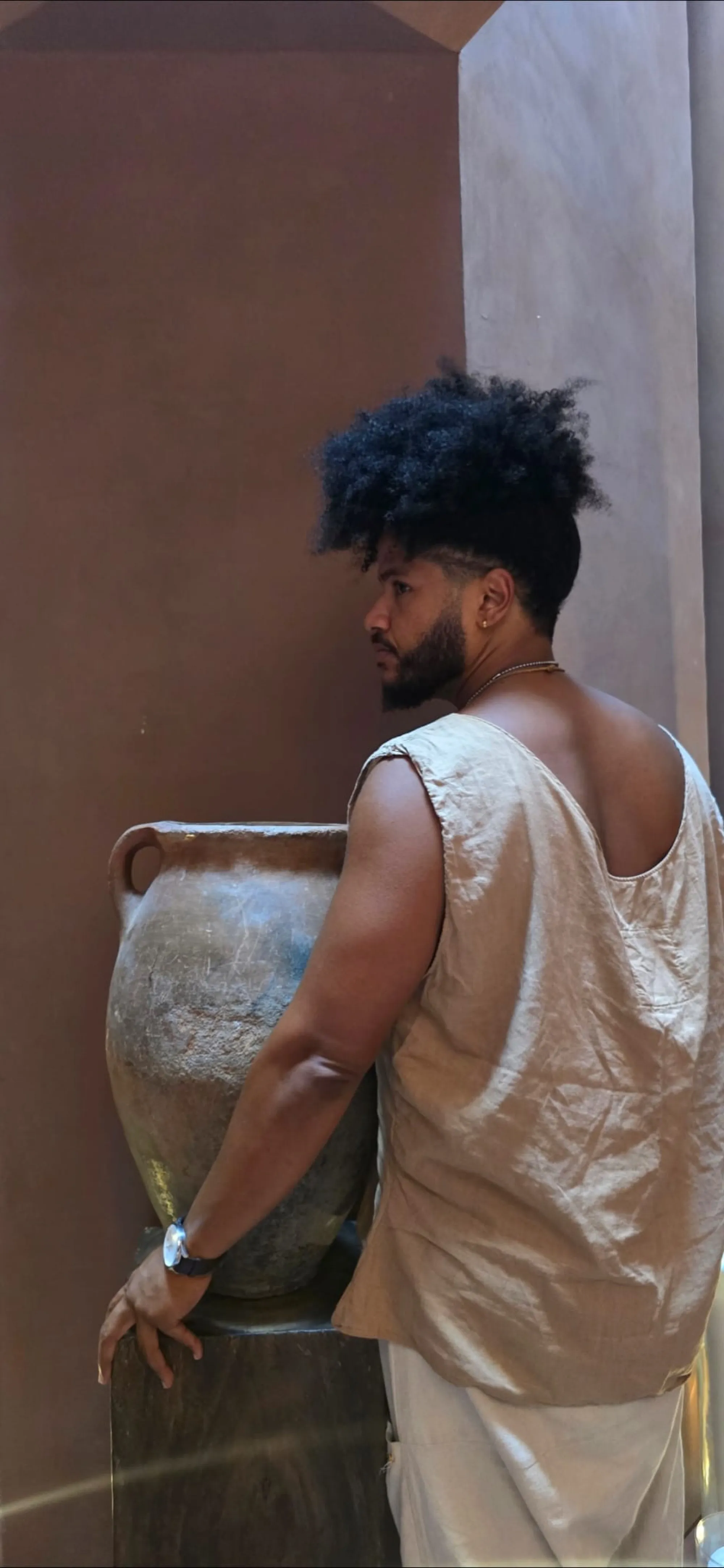 Benjamin Urbaez in profile view leaning against ancient clay vessel, contemplative portrait of global touring musician