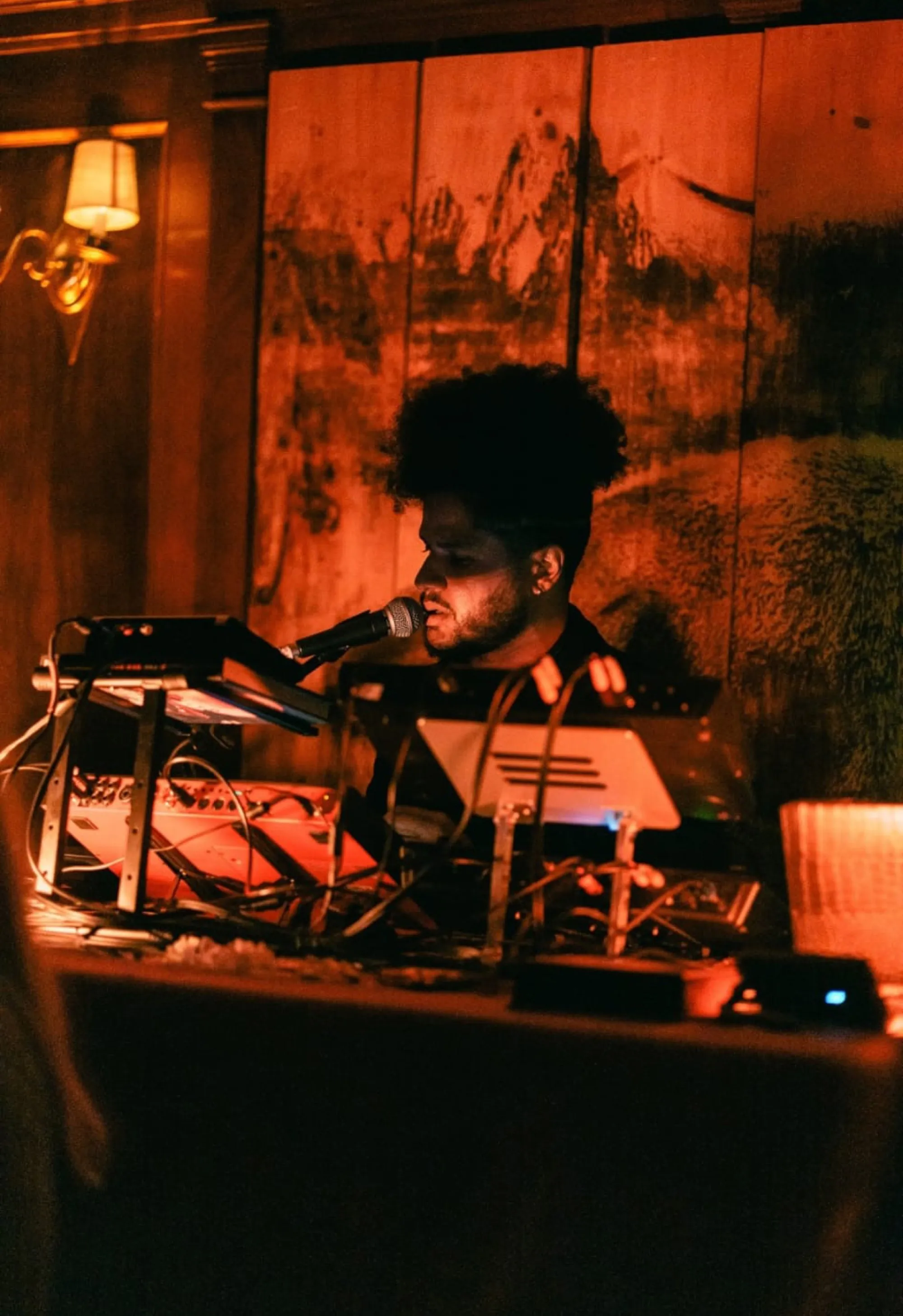 Benjamin Urbaez performing spoken word into microphone with warm amber lighting at live spiritual music event